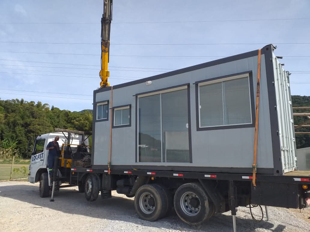 Mini casa cinza sendo transportada por caminhão munck